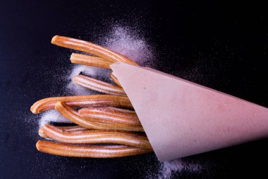 Churros taze sıcak yapışır. Koyu arkaplanda kağıt torbada şeker var.