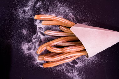 Churros taze sıcak yapışır. Koyu arkaplanda kağıt torbada şeker var.