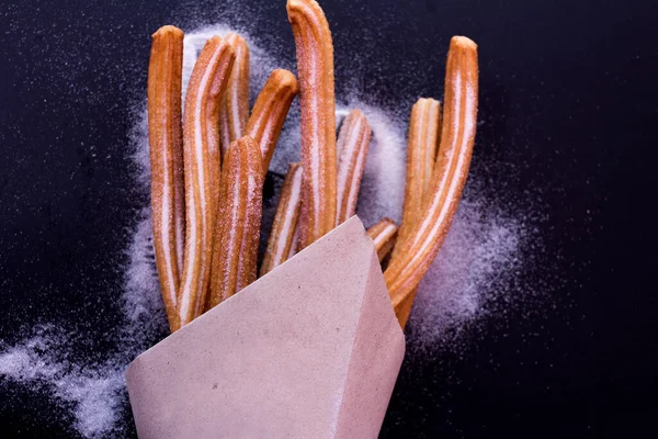 Churros taze sıcak yapışır. Koyu arkaplanda kağıt torbada şeker var.