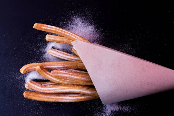 Churros taze sıcak yapışır. Koyu arkaplanda kağıt torbada şeker var.