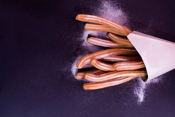Churros taze sıcak yapışır. Koyu arkaplanda kağıt torbada şeker var.