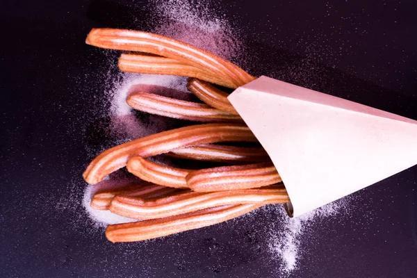 Churros taze sıcak yapışır. Koyu arkaplanda kağıt torbada şeker var.