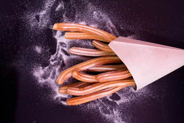 Churros sticks fresh hot with sugar in paper bag on dark background