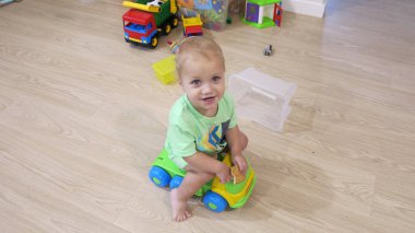 Çocuk oyuncaklarının arka planında arabada oturan küçük sarışın çocuk.