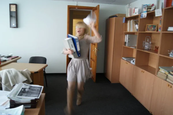 Sarı saçlı bir kız ofiste koşuyor ve kağıtları havaya fırlatıyor.