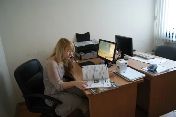 Sarı saçlı bir kız bilgisayarın başına oturur ve telefonda konuşur, iş ilişkilerine karar verir.