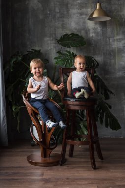Küçük neşeli sarışın çocuklar sandalyeye oturur ve gülerler.