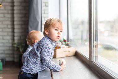 Küçük sarışın çocuk pencereden gömleğiyle dışarı bakıyor.