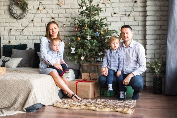 family (mom, dad, two sons) sit on the carpet near the decorated Christmas tree and have fun, waiting for the holiday. happy family, they give each other gifts