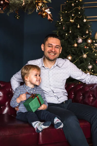 Çocuk mutlu ve gülümsüyor çünkü Noel hediyesi olarak babasından bir hediye, bir oyuncak ve bir araba aldı. Çocuk mutlu çocuk tatil için bekliyor, baba gülümsüyor. Avrupalı aile. Baba ve oğul. Mutlu tatiller.