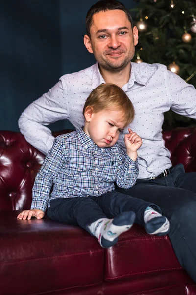 the child is sad because he is waiting for a gift, a toy, a car from his father as a gift for Christmas. The boy is frowning, the boy is upset, the boy is waiting for the holiday, the father is smiling. European family. Father and son