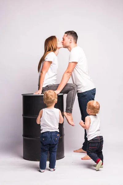Anne bir fıçıya oturur ve babayı öper, çocuklar onun yanında eğlenir. Mutlu Avrupalı aile birlikte vakit geçiriyor, aile mutlu. Anne, baba, oğul, iki oğul, gülümseyen ve dalga geçen, çılgın bir eğlence. Aileyle vakit geçirmek. Beyaz tişörtler ve kotlar.