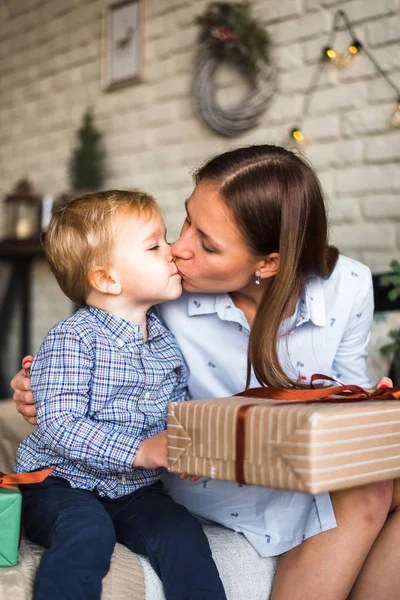 mother gives a Christmas gift to a child and the child gives a kiss on the lips mom