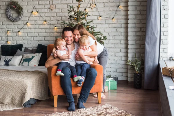 Anne, baba ve iki oğul Noel zamanı turuncu bir sandalyede oturup birbirlerine sarılırlar ve gülümserler.