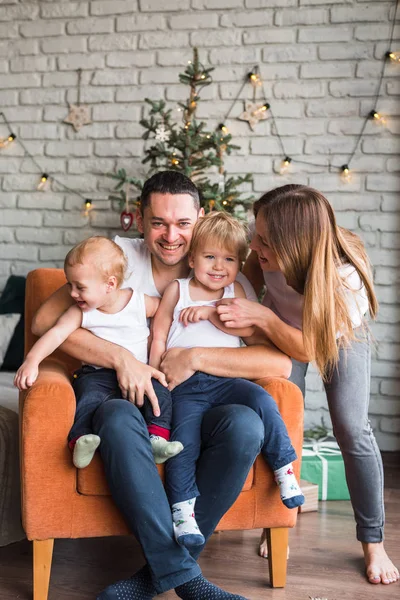 Anne, baba ve iki oğul Noel zamanı turuncu bir sandalyede oturup birbirlerine sarılırlar ve gülümserler.