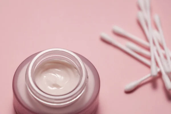Teneke kutuda kozmetik kremi ve pembe arka planda pamuk çubukları.
