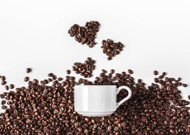 Kahve aşığı konsepti. Kahve çekirdeklerinden yapılmış kalpler ve arka planda beyaz bir kupa.