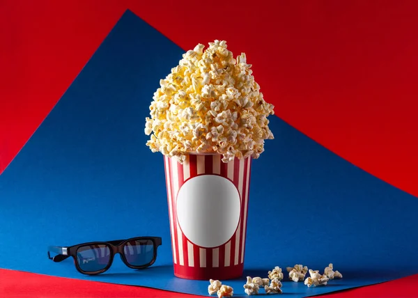 Sinema kompozisyonu bir sepet patlamış mısır ve 3D bardaktan yapılır. Kırmızı ve mavi arkaplan.