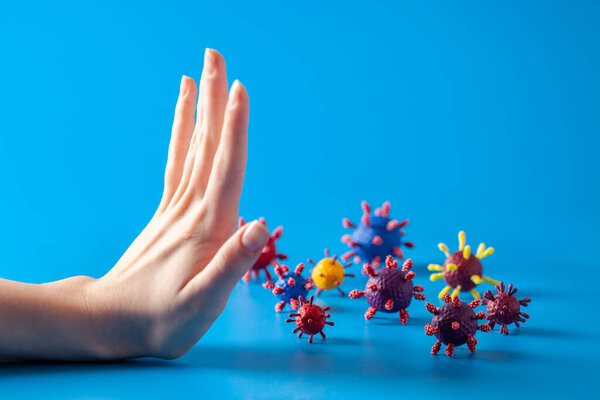 Stop epidemic concept. COVID-19 Pandemic Coronavirus. Woman hand and artificial models of viruses on a blue background.