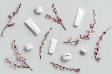 Kozmetik deseni. Açık gri bir zemin üzerinde kozmetik kapları ve kavanozlardan ve bahar çiçeklerinden oluşan kompozisyon.