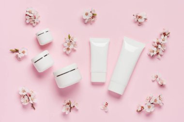 Güzellik arka planı. Konteynırlardan, kozmetik kavanozlarından ve pembe arka plandaki bahar çiçeklerinden oluşan bir kompozisyon. Düz yatıyordu. Üst görünüm.