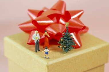 Minyatür aileler ve küçük oğulları Noel 'i bir hediye kutusunun üstünde kutluyorlar.