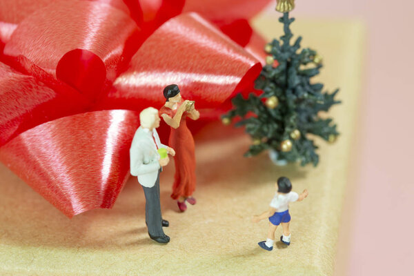 Miniature Parents celebrating christmas with their little boy on top of a gift box with a red ribbon