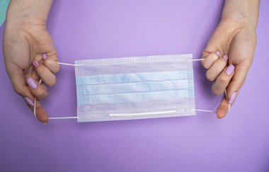 Kadının elleri mavi bir tıbbi maske tutuyor. Renkli arka plan. Kişisel tecrit