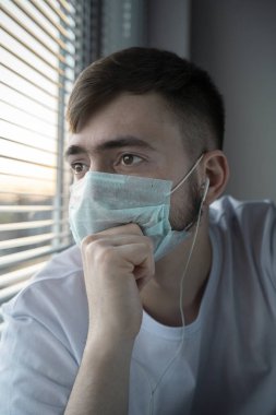 Genç adam gün batımında pencereden dışarı bakar. Kulaklıkla telefonla konuşuyor. Kişisel izolasyon