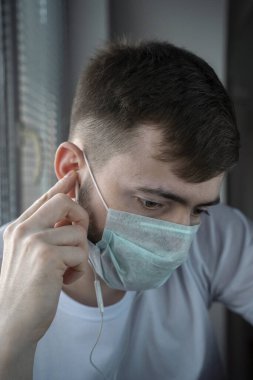 Gün batımında tıbbi maskeli genç bir adam pencereden dışarı bakar. Kulaklıklarla. Kişisel tecrit.