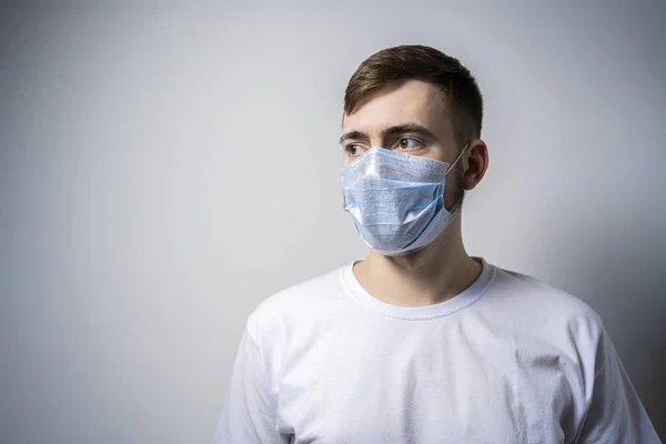 A young man in a medical mask on a white background looks away. Self isolation