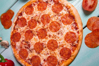 Turkuaz arka planda Pepperoni pizza. Masada domates, sosis ve kırmızı biber..