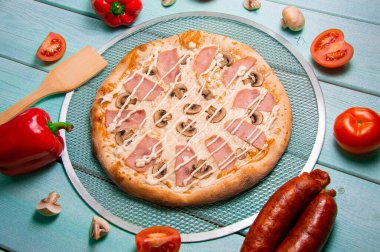 Peynirli pizza, jambon ve turkuaz arka planda mantar. Tahta spatula. Kırmızı biber. Menü için fotoğraf.