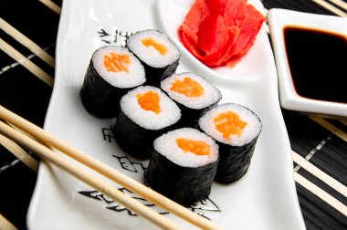 Beyaz tabakta kırmızı balıklı rulo. Çin yemek çubukları. Beyaz bardakta soya sosu..