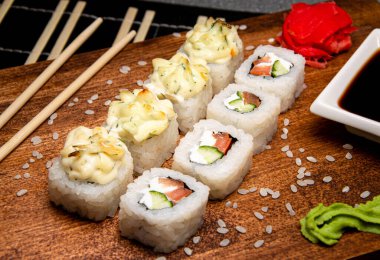 Tahta bir tahtanın üzerinde sebzeli ve peynirli dürüm. Çin yemek çubukları. Beyaz bardakta soya sosu..