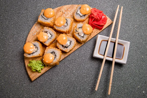 Set of baked rolls on a brown tray. Photo for the menu. A cup with sauce. Chinese chopsticks