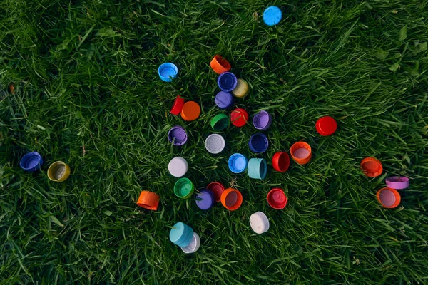 Plastic bottle caps on a green lawn. Garbage collection. Bright objects