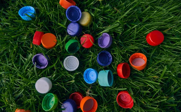 Plastic bottle caps on a green lawn. Garbage collection. Bright objects