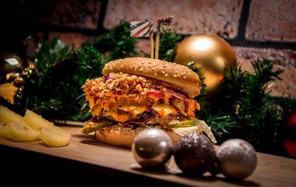 Ananaslı Noel burgeri. Tuğla duvar ve Noel ağacının arka planında bir burger. Ön planda Noel oyuncakları.