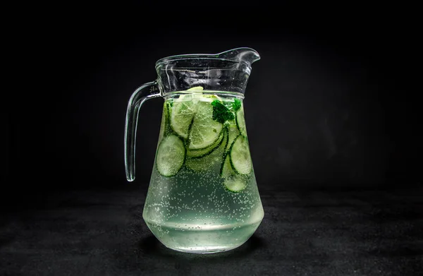 natural lemonade with cucumber, mint and ice. a soft drink in a jug on a black, isolated background . carbonated water with syrup