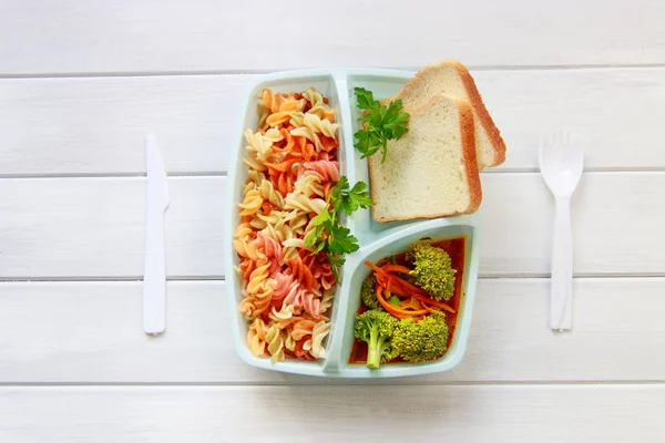 Green school lunch box with pasta, broccoli and carrot close up