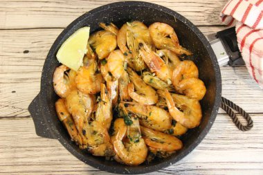 Limonlu kızarmış karides ve gri bir masada küçük bir tavada otlar.