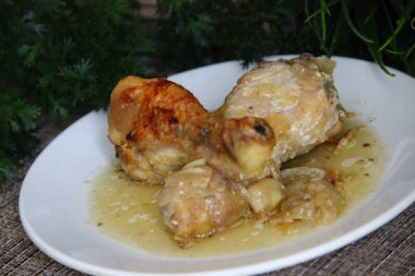 Pişmiş tavuk budu (kavrulmuş bacaklar) ve yeşillik arka planında beyaz bir tabakta soğan sosu. Biraz yakın.