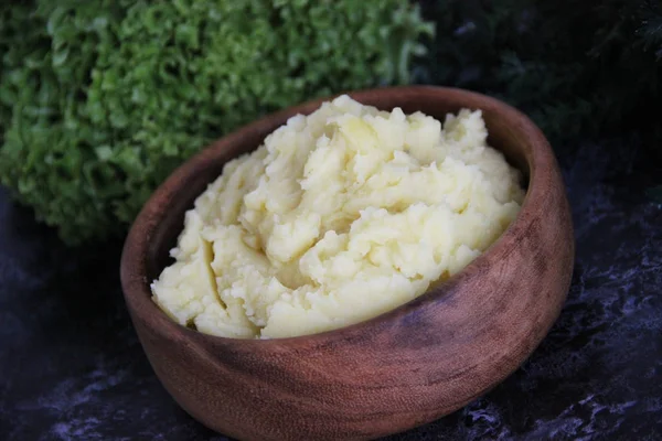 Siyah mermer bir masanın üzerinde patates püresi olan ahşap yuvarlak bir kupa taze yeşilliğin arka planına karşı. Patates püresi.