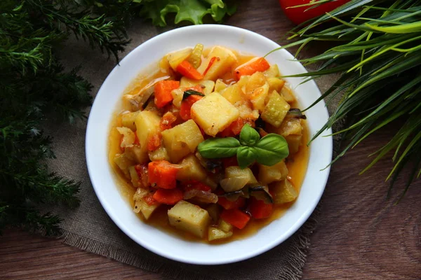 Vegetable stew with a Basil leaf on a white flat plate surrounded by greenery on all sides, enhanced photo effect