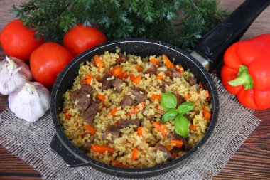 Taze sebzelerin arka planında keten peçetede et ve havuç dolu bir tavada bulgur pilavı.