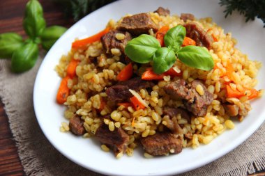 Beyaz bir tabakta et ve havuçla Basil yaprağıyla bulgur pilavı.