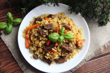 Beyaz bir tabakta et ve havuçla Basil yaprağıyla bulgur pilavı.