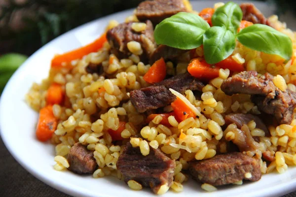 Bulgur pilaf with meat and carrots on a white plate with a Basil leaf