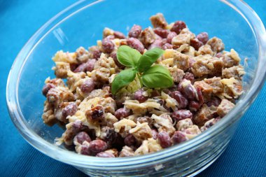 Mavi arka planda şeffaf bir kasede konserve fasulye, peynir ve istiridye salatası.